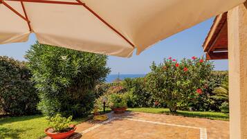 A garden patio with potted plants, a tiled floor, and a view of the sea.