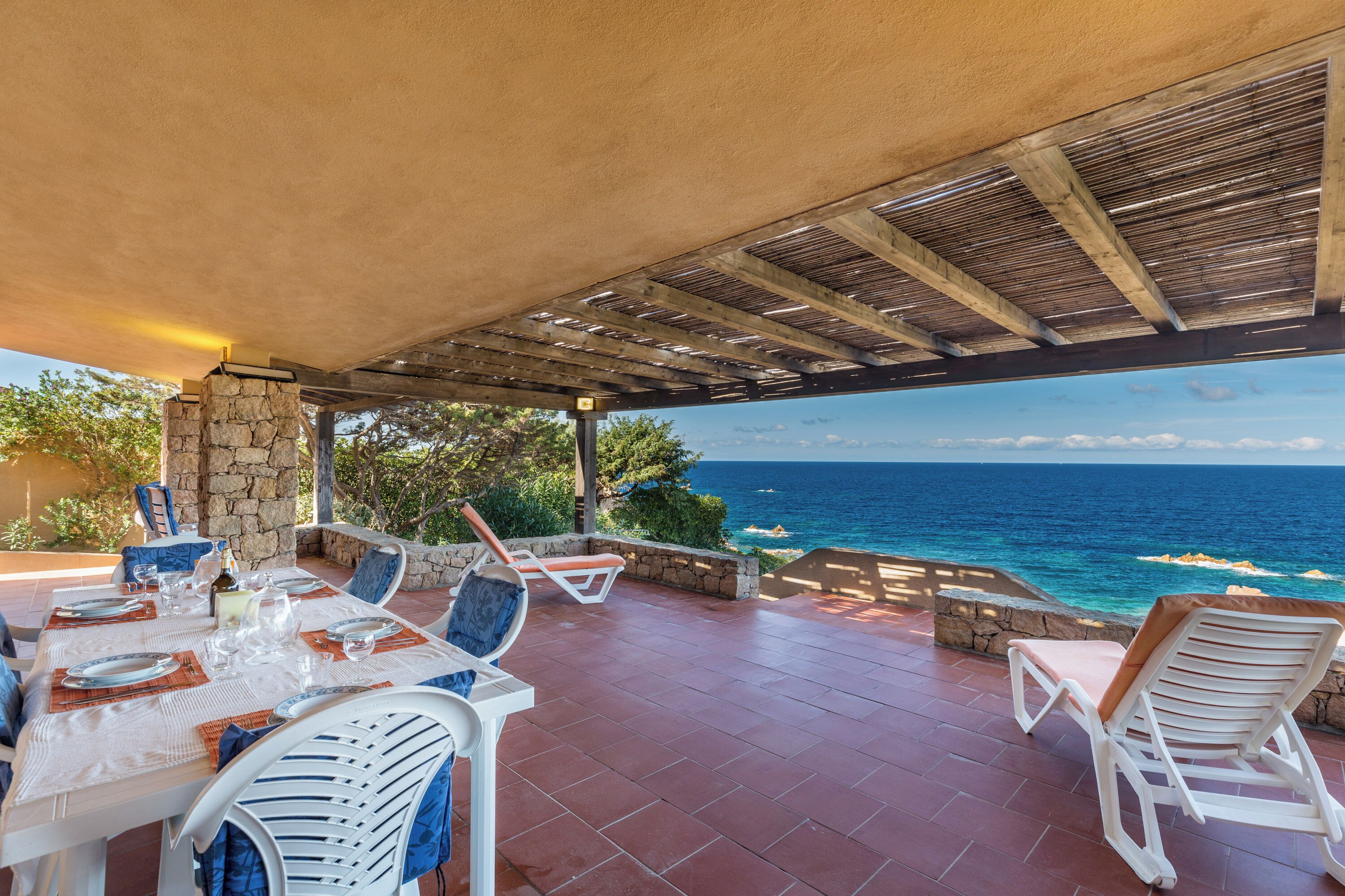 Zona pranzo all'aperto con vista sull'oceano, pareti in pietra e una pergola.