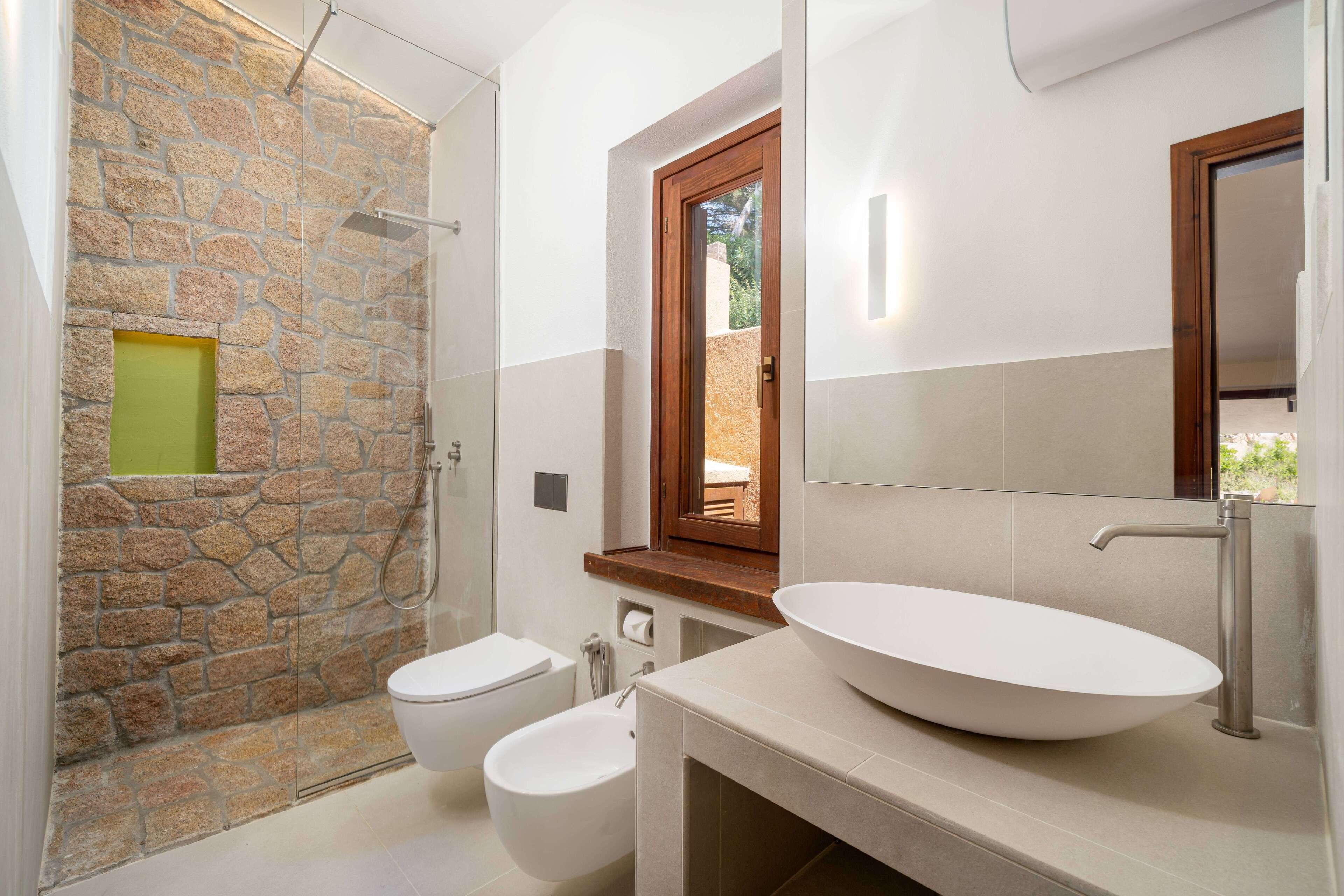 Une salle de bain avec une douche à l’italienne en pierre, un lavabo blanc doté d’un grand bac et des toilettes.