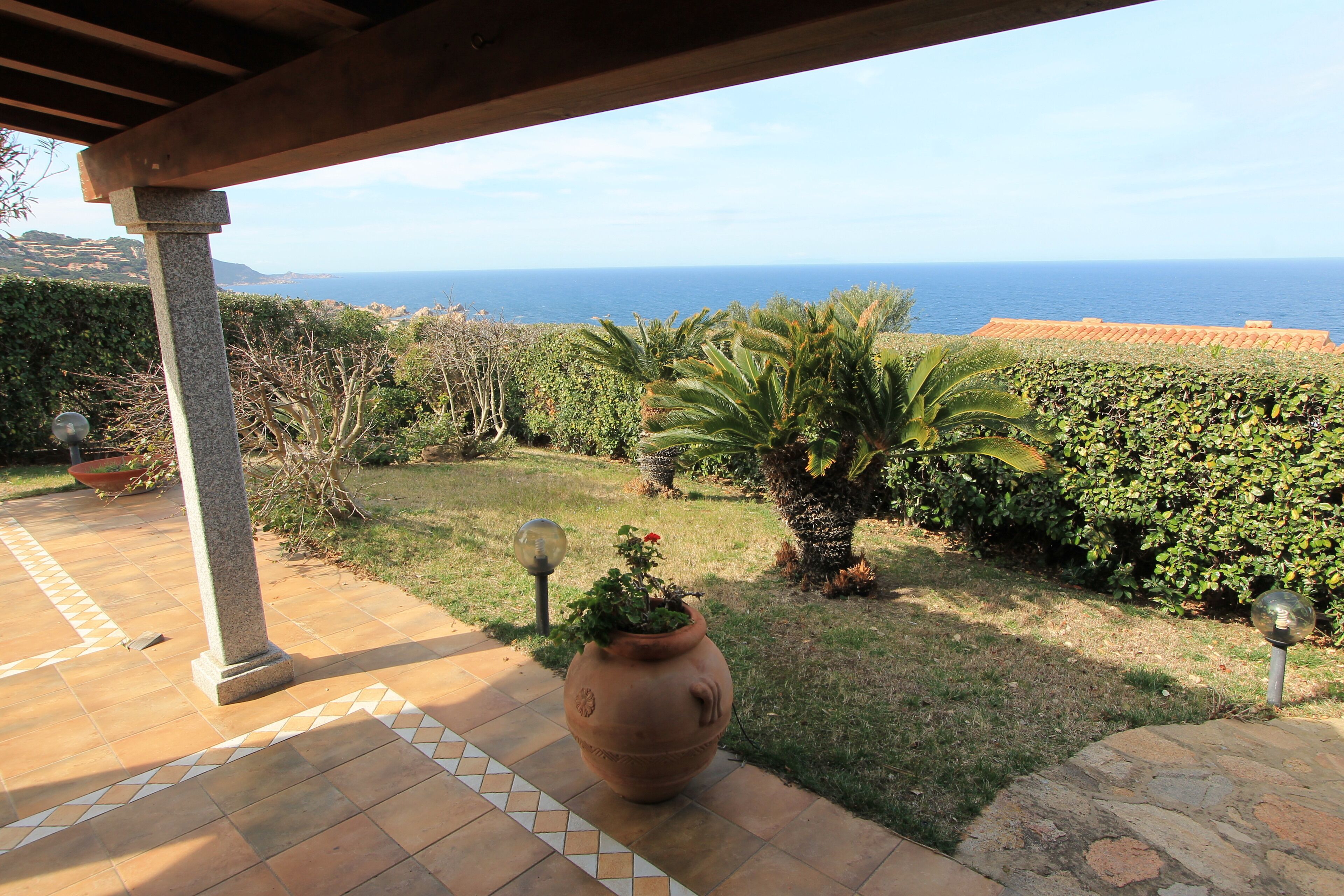 Um pátio com vista para o oceano, um vaso de terracota grande e uma estrutura de pérgola.