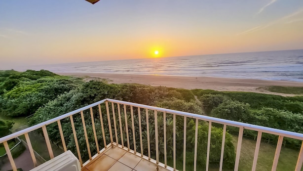 Een balkon met uitzicht op de oceaan bij zonsondergang.