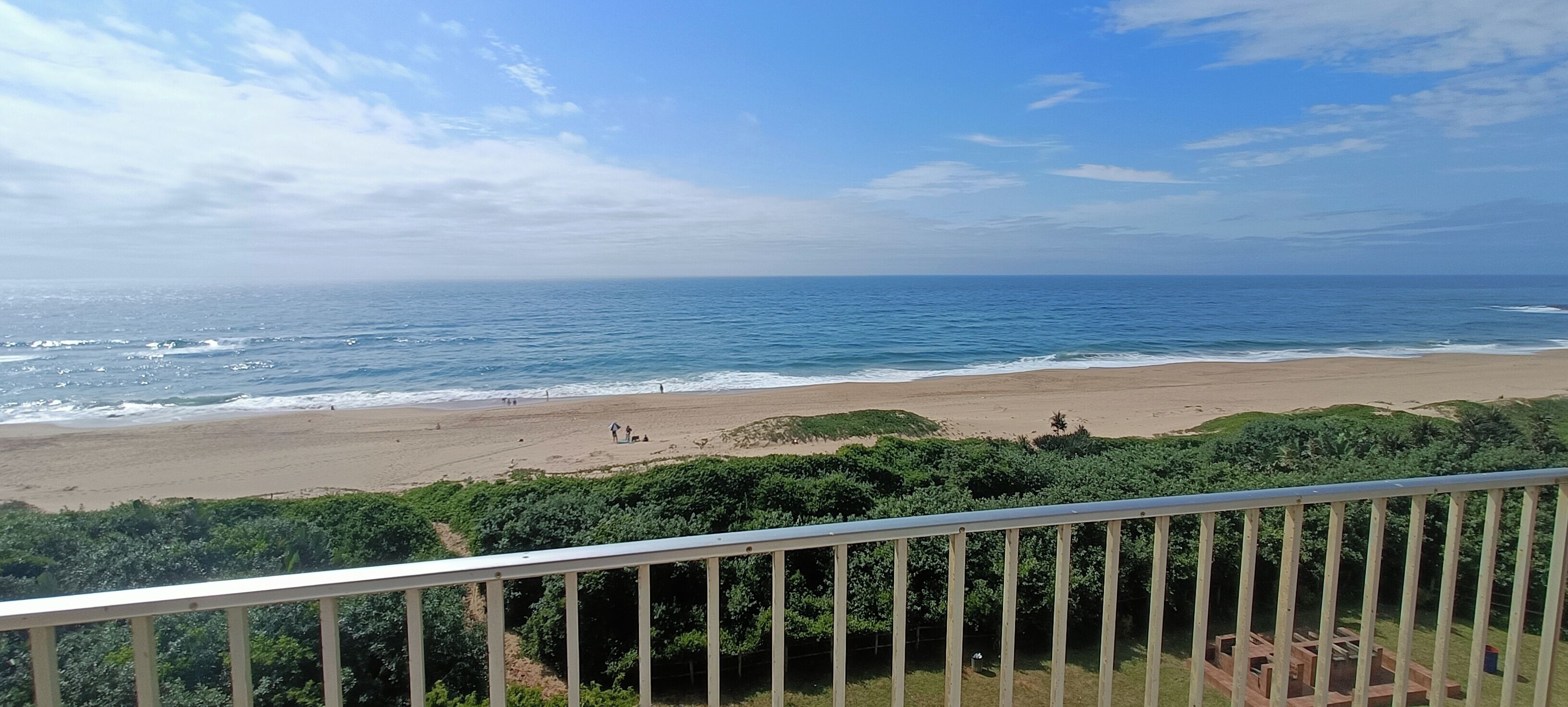 Vista da praia a partir de uma varanda com grades, oceano e vegetação.