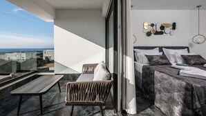 A balcony with a view of the city, a bed with a grey bedspread, and a wall-mounted light fixture.