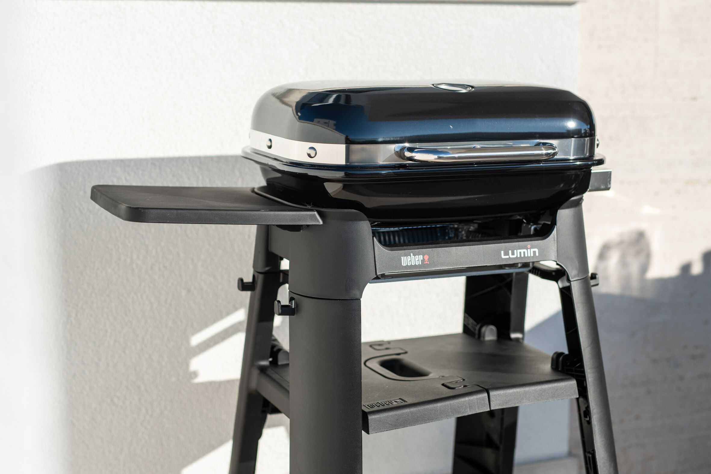 Una griglia Weber Lumin portatile con finitura nera, un manico laterale e un pannello di controllo frontale.