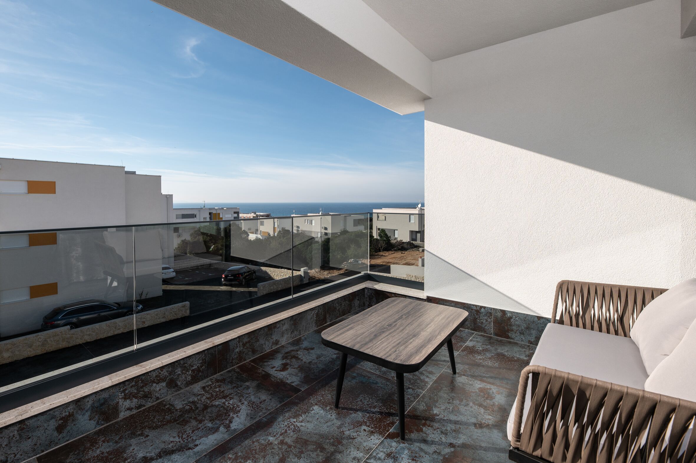 Een modern balkon met glazen balustrade, een houten tafel en een stoel met kussens.