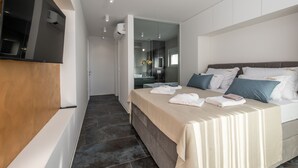 A modern hotel room with a large bed, a TV mounted on the wall, and a bathroom visible through a glass door.