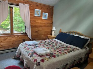 Ein Schlafzimmer mit einem hölzernen Kopfteil, einer gesteppten Bettdecke, einem Nachttisch mit Lampe und einem Fenster mit Vorhängen.