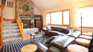 A living room with a stone fireplace, a leather sofa, a staircase, and a large window. - Pet Friendly Private Waterfront home, Estates (Campton)