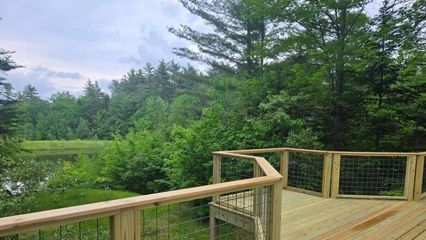 A wooden deck with a metal railing overlooking a forested area. - Pet Friendly Private Waterfront home, Estates (Campton)