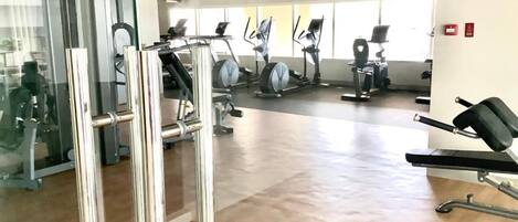 A gym with various exercise equipment, including treadmills and weight machines, and a wooden floor.