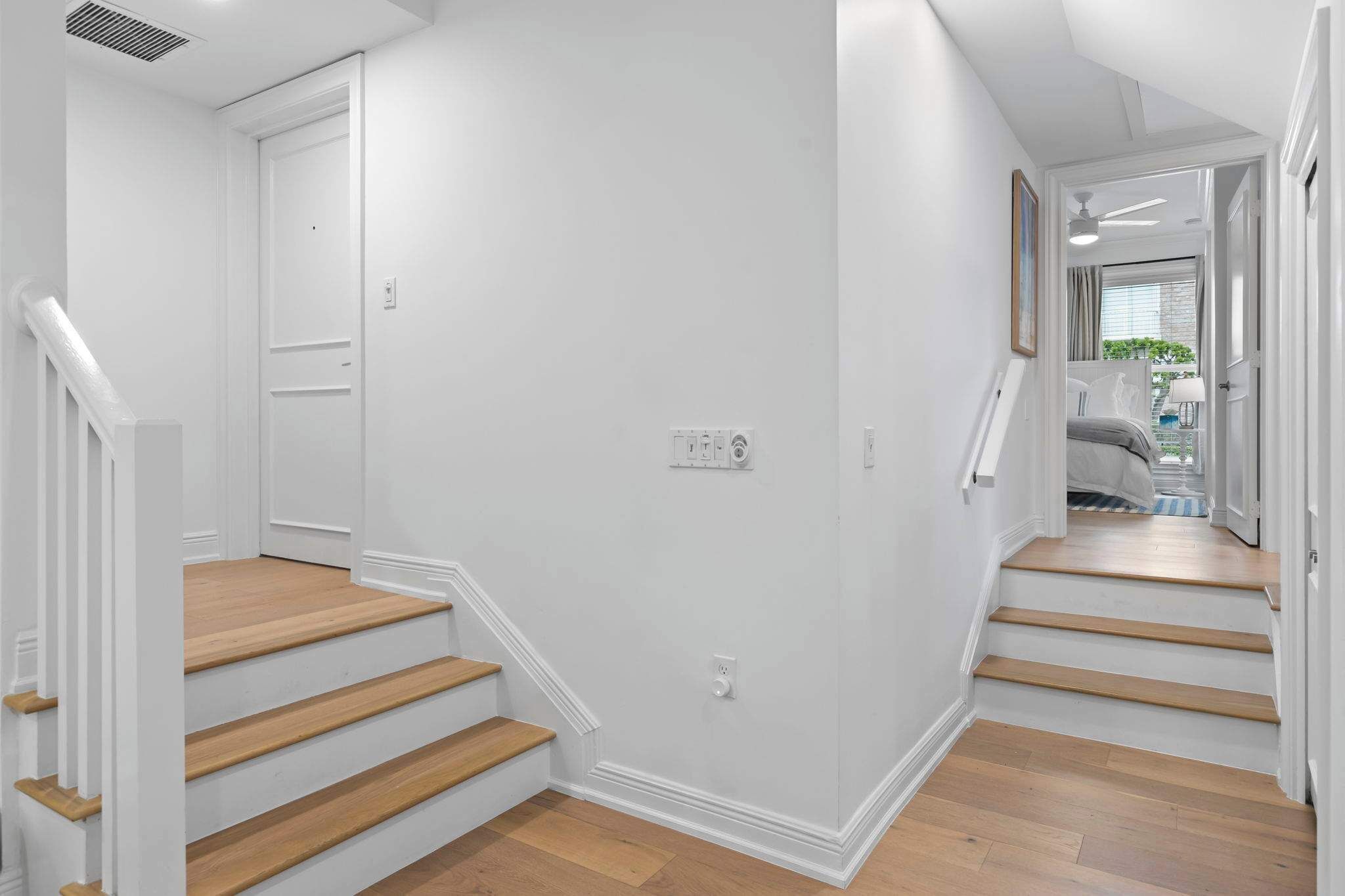 A clean, white-walled hallway with wooden stairs leading to a bedroom.