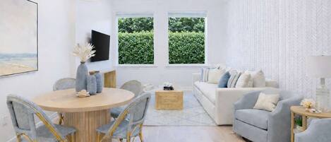Una sala de estar moderna con una mesa de comedor redonda, sillas tapizadas en gris, un sofá gris y una pared blanca con estampado.