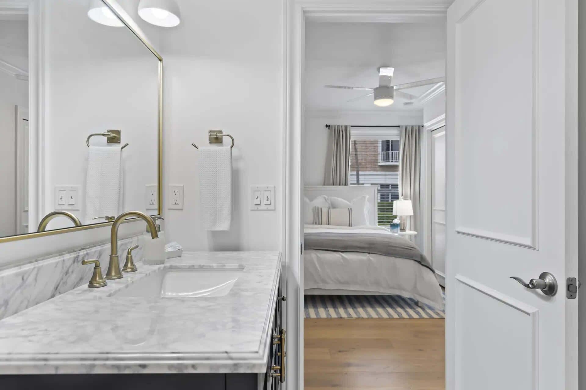 A modern bathroom with a marble sink, gold fixtures, and a large mirror.