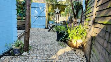 A garden with a gravel path, potted plants, a wooden fence, and a blue gate.