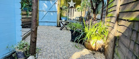A garden with a gravel path, potted plants, a wooden fence, and a blue gate.