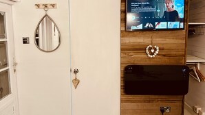 Kylpyhuoneessa on valkoinen ovi, peili, sydämenmuotoinen koriste-esine, puiseen seinään asennettu televisio ja musta laite lattialla.