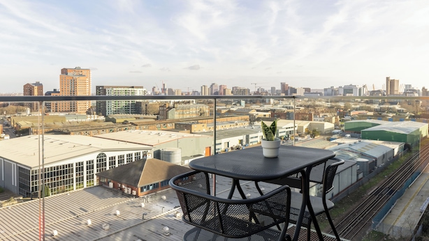 Una terraza en la azotea con una mesa y sillas, una planta en maceta y vistas panorámicas de la ciudad.
