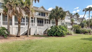 A row of coastal-style houses with a well-maintained lawn and palm trees. - Award-Winning Resort Amenities | Commons Court 3 (Isle of Palms)