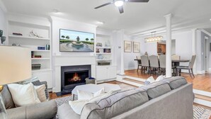 A modern living room with a fireplace, a ceiling fan, and a dining area with a chandelier. - Award-Winning Resort Amenities | Commons Court 3 (Isle of Palms)