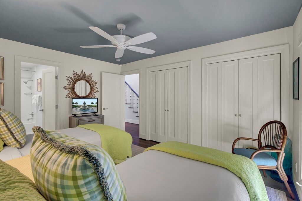 A bedroom with two beds, a ceiling fan, a TV, and a chair.