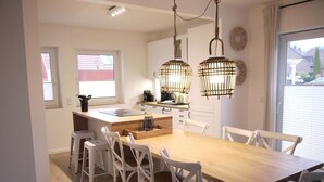 A modern kitchen with a wooden island, white chairs, and pendant lights. - Großzügige Wohnung auf 125qm mit Terrasse, Wintergarten, Sauna und Kamin (Scharbeutz)