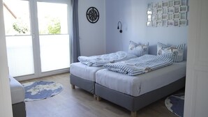 A bedroom with a double bed, a small seating area, a large window with curtains, and a wall with framed pictures. - Großzügige Wohnung auf 125qm mit Terrasse, Wintergarten, Sauna und Kamin (Scharbeutz)