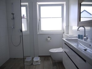 A modern bathroom with a glass shower enclosure, a toilet, and a sink with a mirror. - Großzügige Wohnung auf 125qm mit Terrasse, Wintergarten, Sauna und Kamin (Scharbeutz)