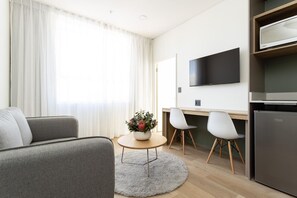 A modern living room with a sofa, a small round table with a vase, and a TV mounted on the wall.