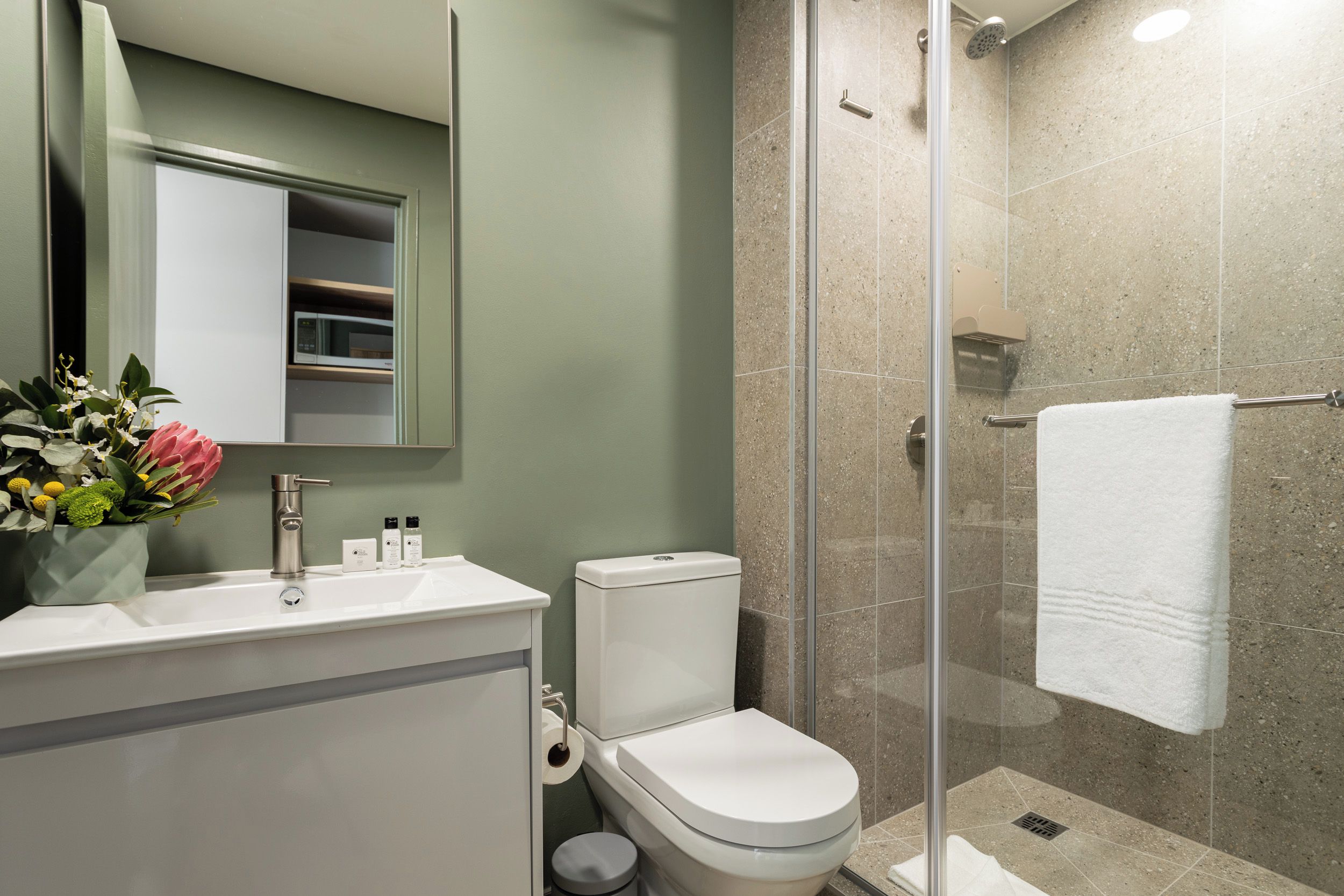 A modern bathroom with a glass-enclosed shower, a white toilet, and a vanity with a mirror and sink.