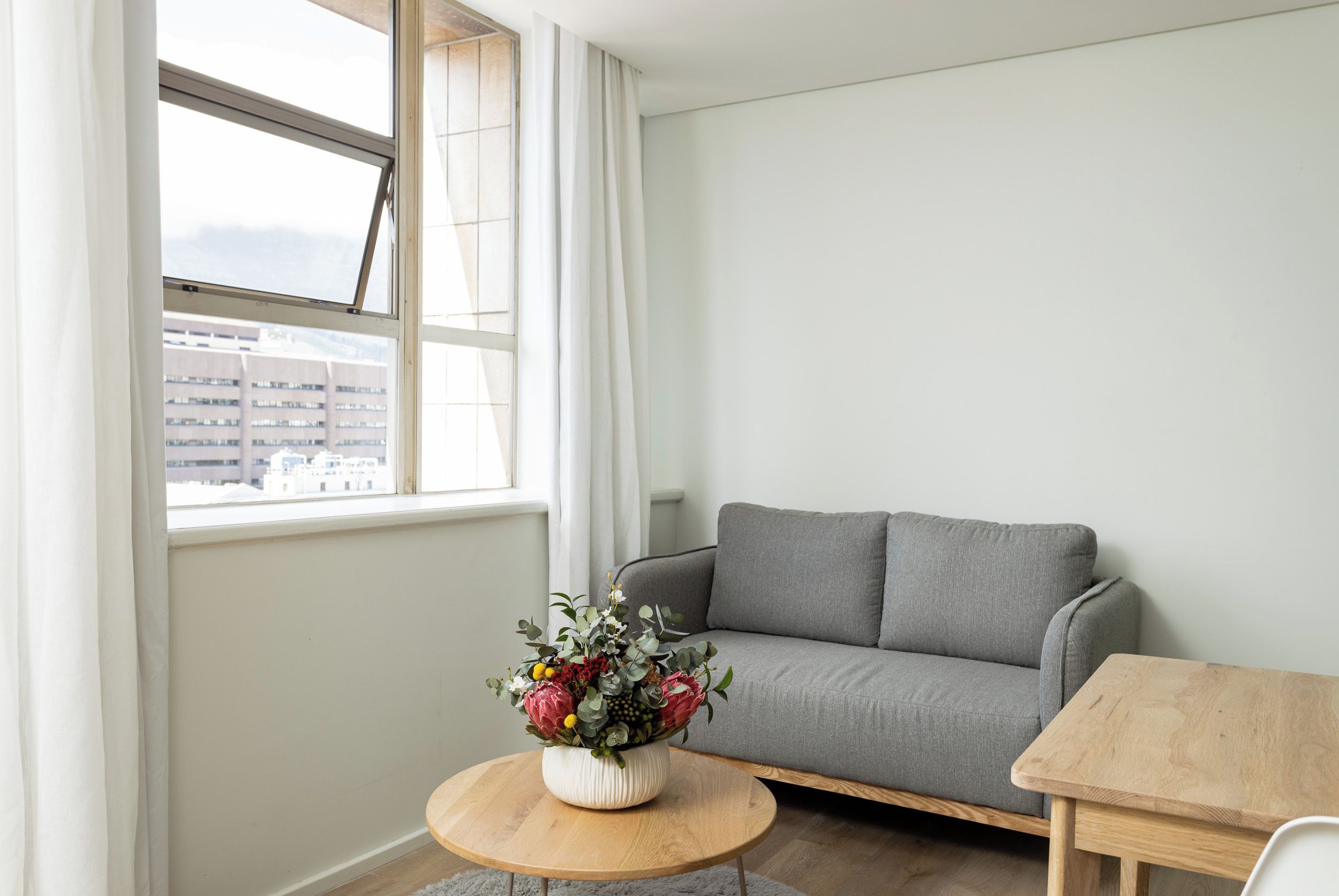A modern living room with a grey sofa, a wooden coffee table, and a window with curtains.