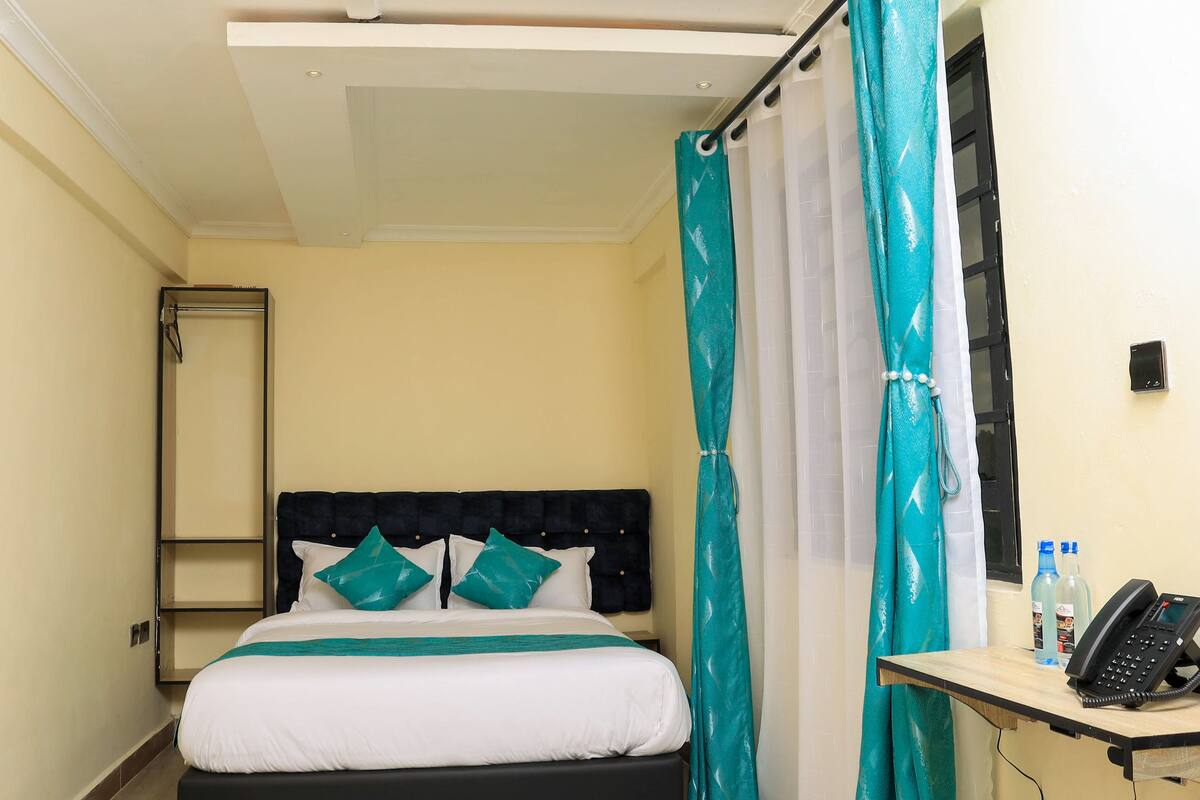 A hotel room with a bed, a bedside table with a phone, and a window with a curtain.