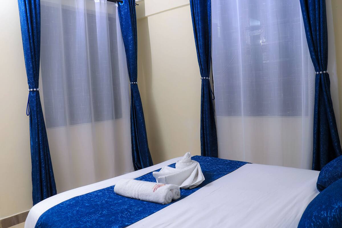 A hotel room with a bed, blue curtains, and a white towel.