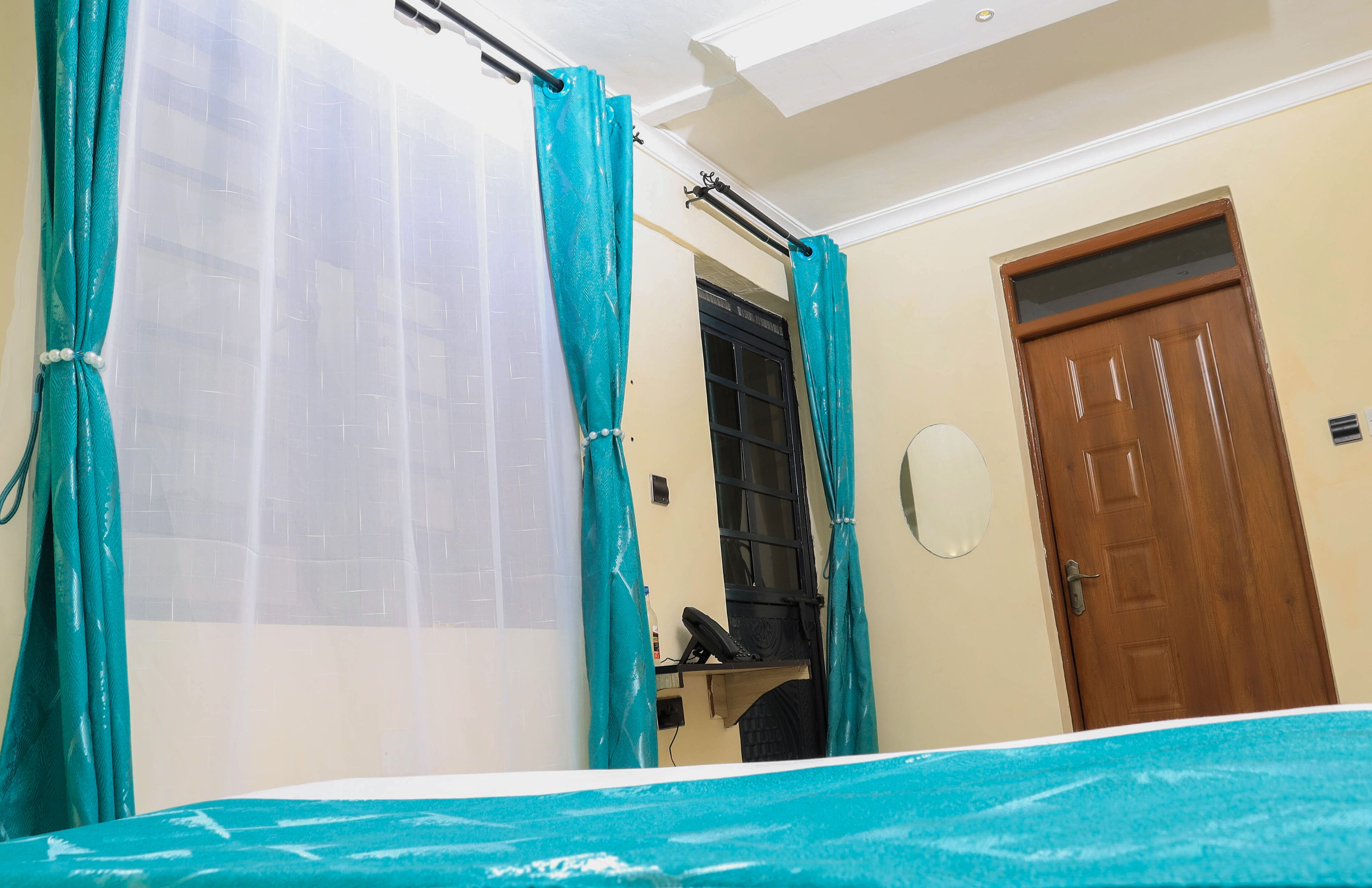Una habitación con cama, puerta de madera y ventana con cortina.