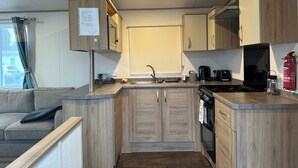 A compact kitchen with wooden cabinets, a sink, a stove, and a coffee maker. - Felixstowe Chimo Caravan 8 Sleeps 5 min to Beach (Felixstowe)