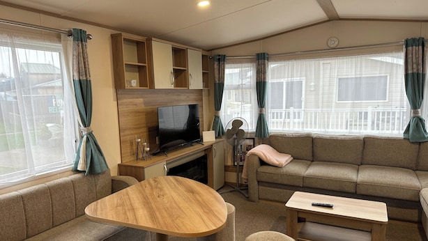 A cozy living area with a sofa, a wooden coffee table, a TV, and a fan. - Felixstowe Chimo Caravan 8 Sleeps 5 min to Beach (Felixstowe)