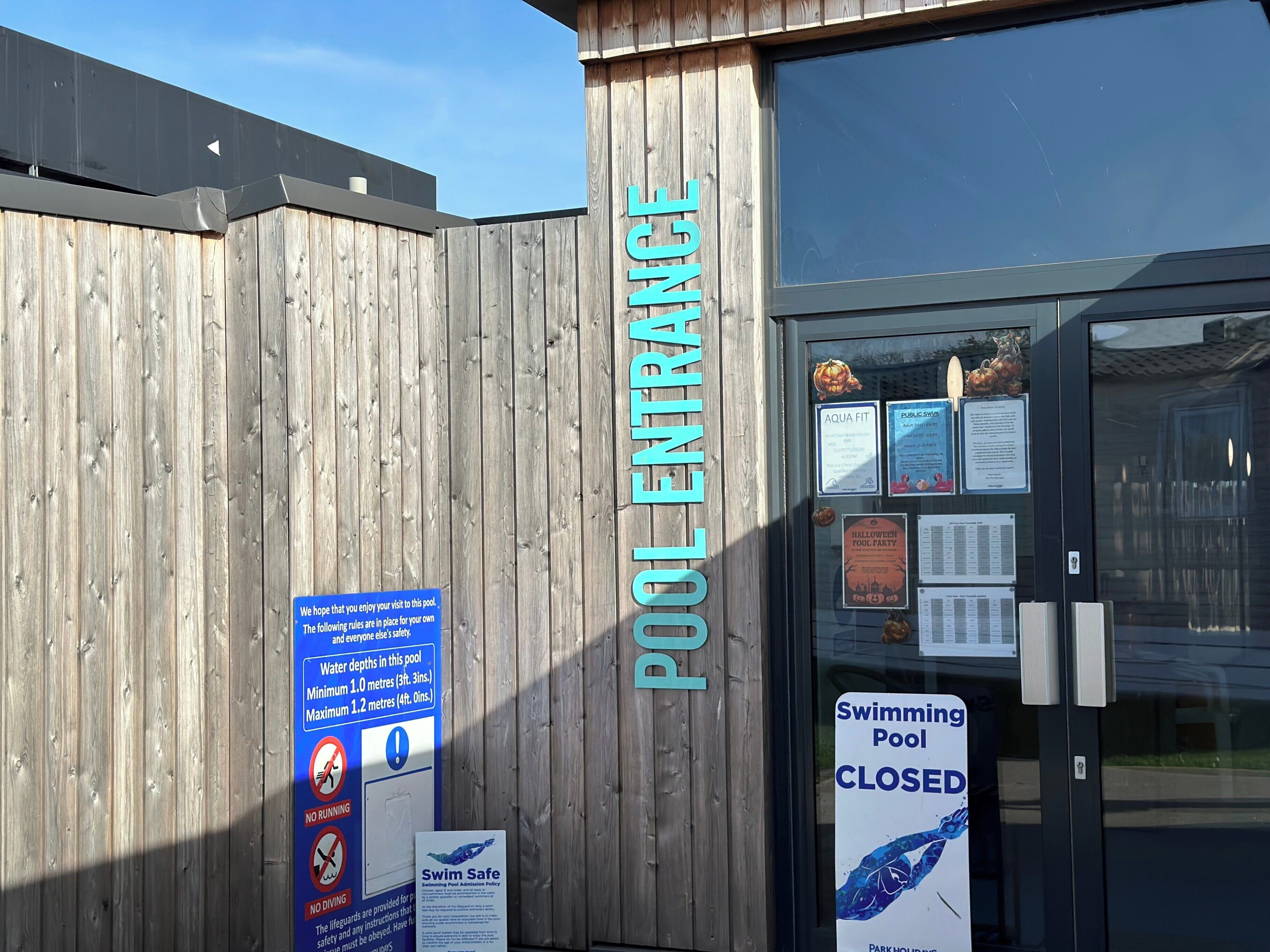 A wooden fence with a sign reading "POOL ENTRANCE" and a closed swimming pool sign.