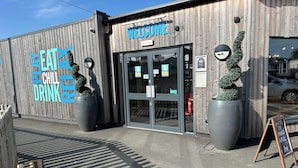 A building with a wooden facade, a 'WELCOME' sign above the entrance, and large planters with topiary. - Felixstowe Chimo Caravan 8 Sleeps 5 min to Beach (Felixstowe)