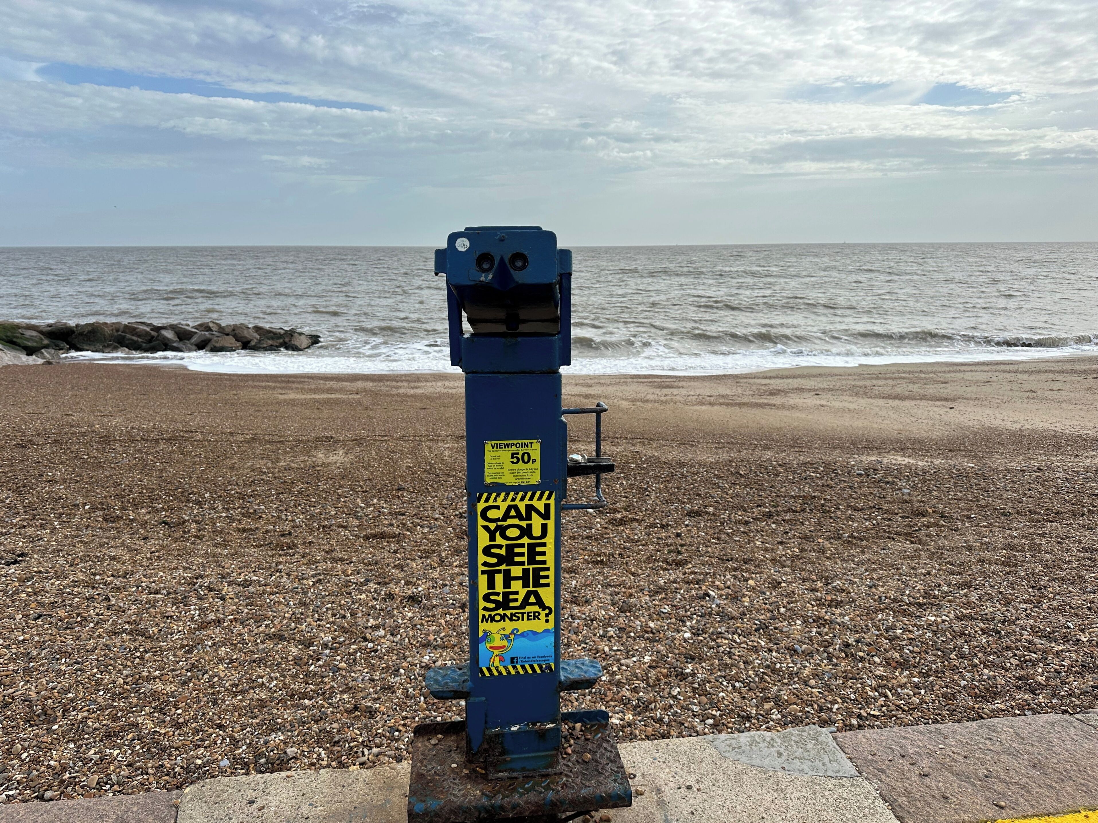 A beach with a blue structure featuring a sign that reads "VIEWPOINT 50p CAN YOU SEE THE SEA MONSTER?"