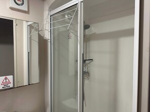 Ein Badezimmer mit Duschkabine aus Glas, einem Warnschild für heißes Wasser und einem Spiegel.