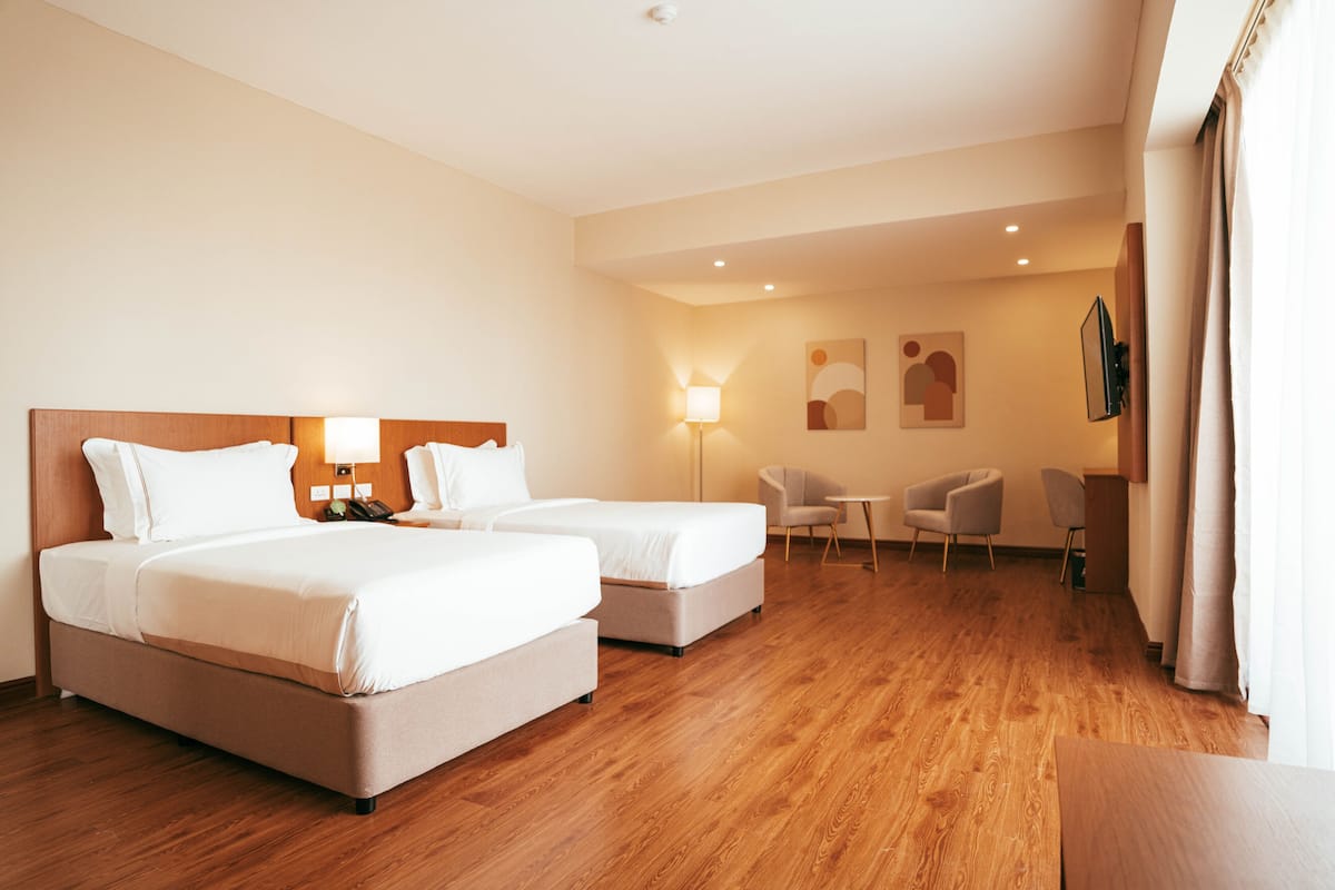 A hotel room with two beds, a desk, a chair, and a TV.