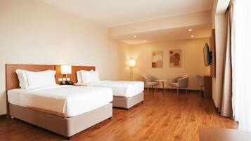 A hotel room with two beds, a desk, a chair, a lamp, and a TV on the wall.