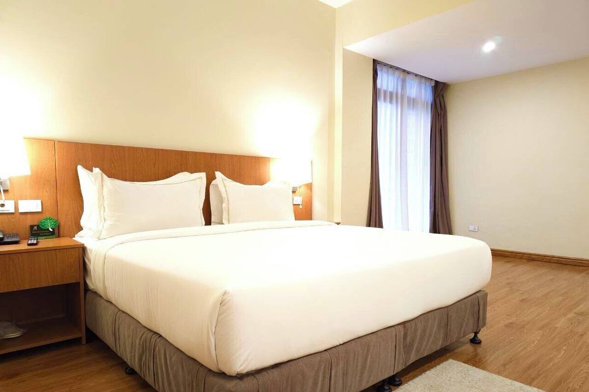 A neatly made bed with a wooden headboard, a bedside table with a lamp, and a window with curtains.