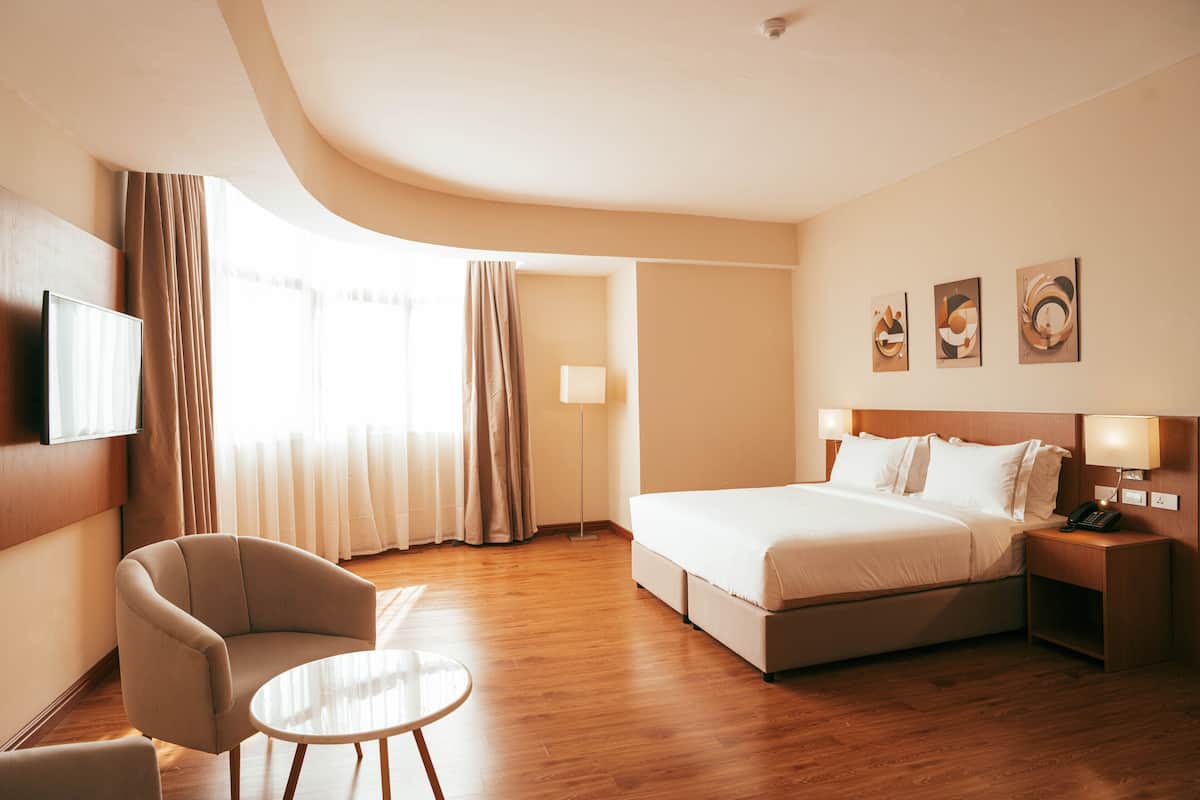 A hotel room with a bed, a chair, a small table, a TV, and artwork on the wall.