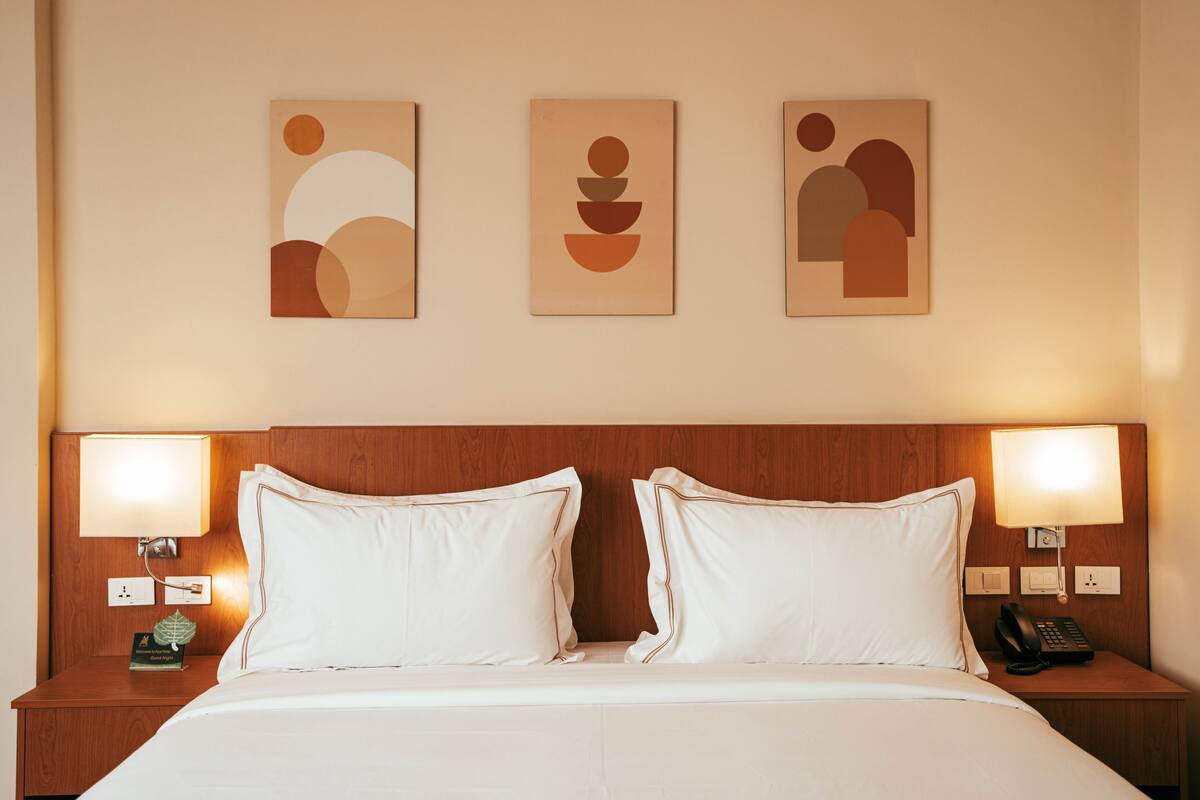A hotel room with a wooden headboard, two bedside lamps, a telephone, and three abstract wall art pieces.