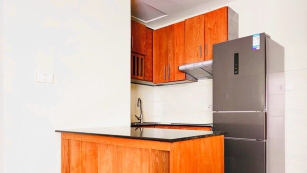 A compact kitchen with wooden cabinets, a stainless steel refrigerator, and a black countertop. - AYA Addis Hotel (Addis Ababa)