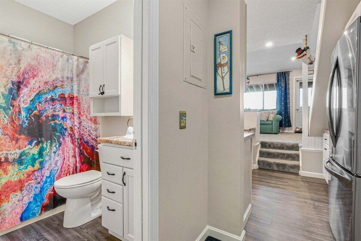 Une salle de bain avec un mur décoré d’un motif abstrait et coloré, des toilettes blanches, un meuble et un rideau de douche.