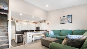 A modern kitchen with white cabinets, a dining area with a green sofa, and a staircase leading to another level.