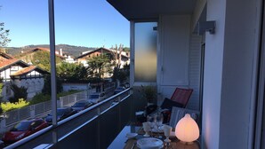Un balcon avec une table dressée pour le dîner, donnant sur une rue bordée de voitures garées et de maisons.