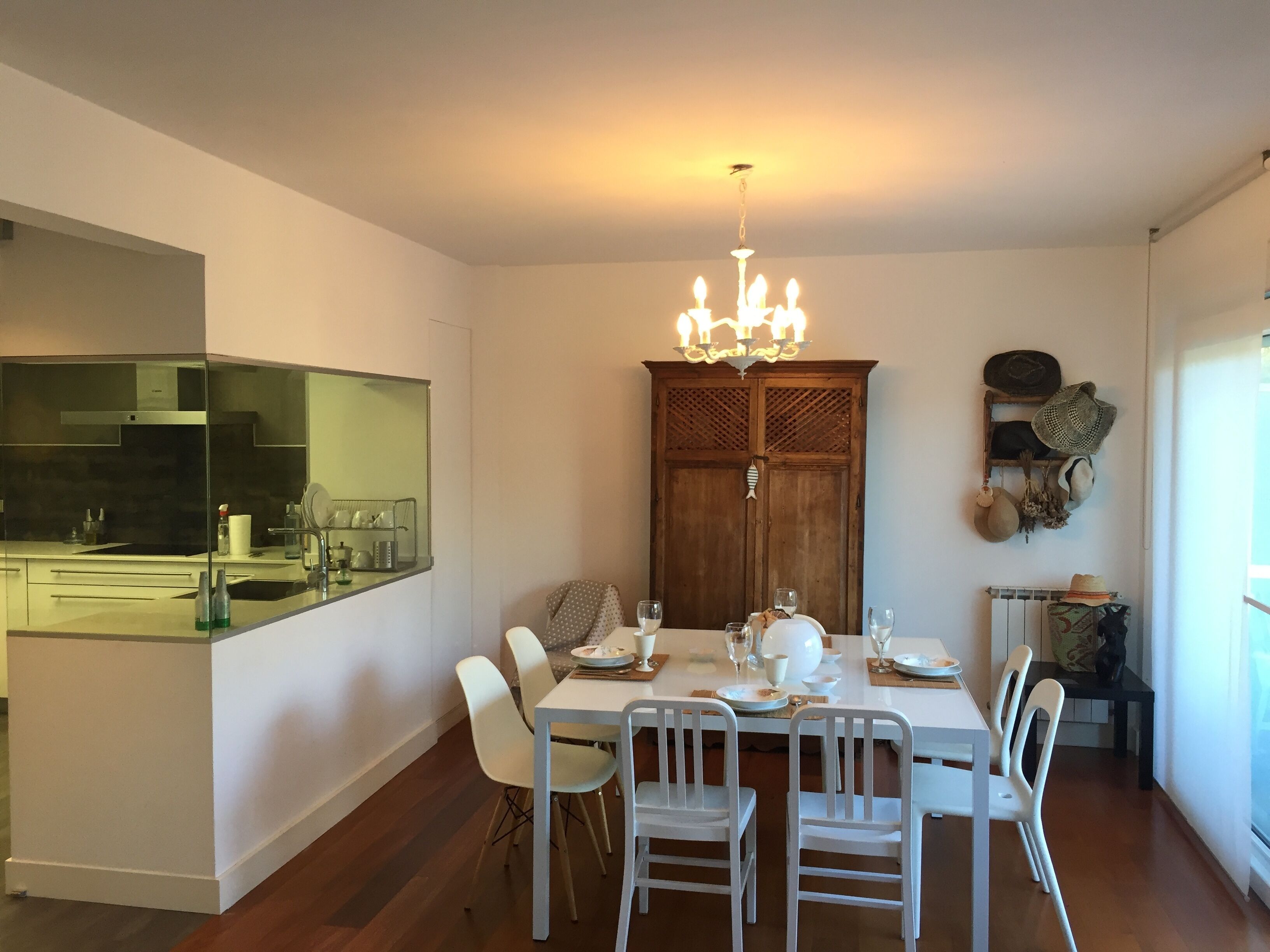 A dining area with a white table set for six, a wooden cabinet with hats, and a chandelier.