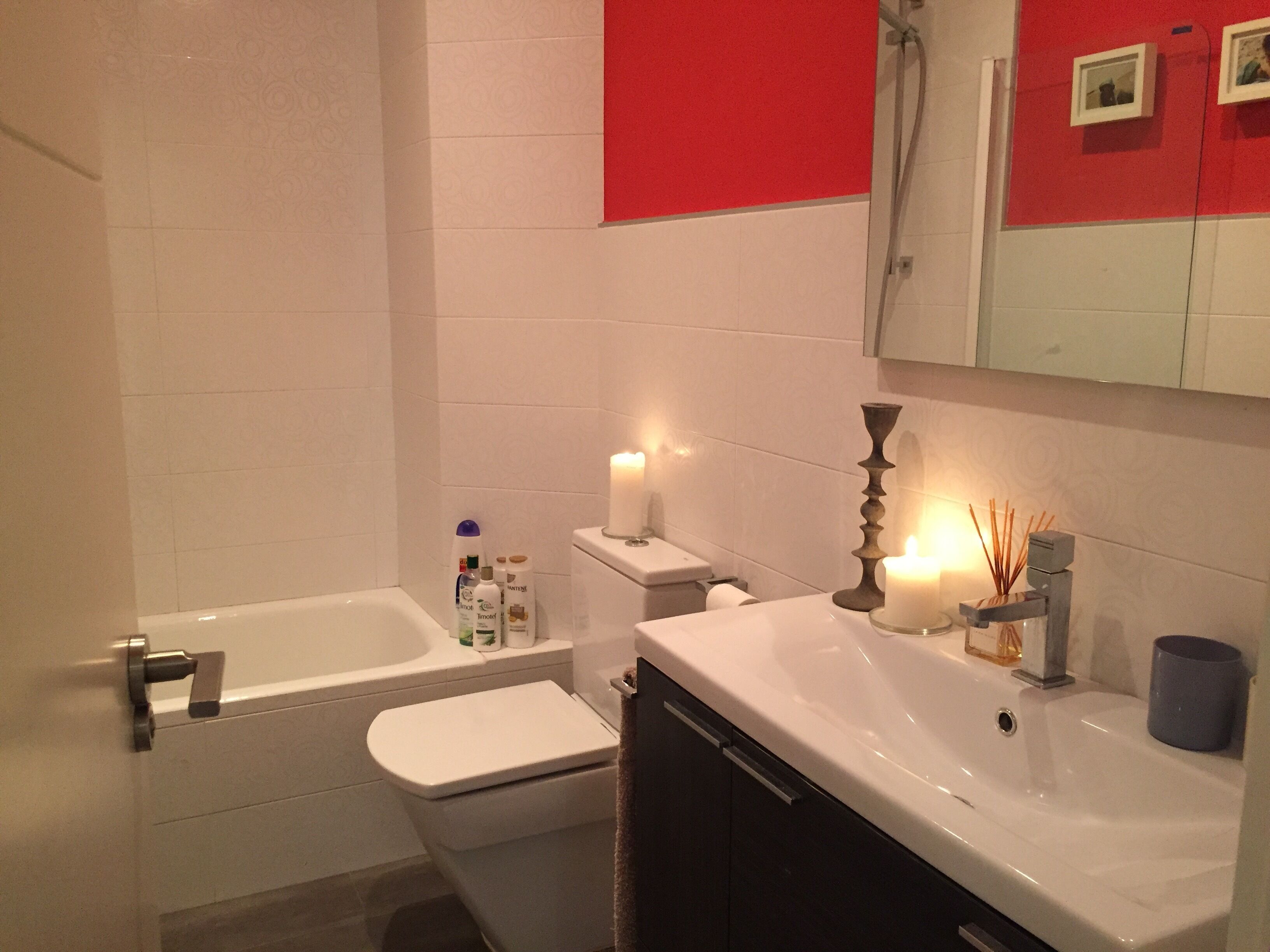 A bathroom with a bathtub, toilet, and sink. There are toiletries on the sink counter, a candle, and a mirror above the sink.